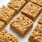 peanut butter rice crispy treats cut into squares on white parchment.