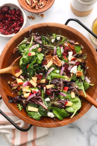 thanksgiving salad tossed with two wooden spoons near a bowl of cranberries.